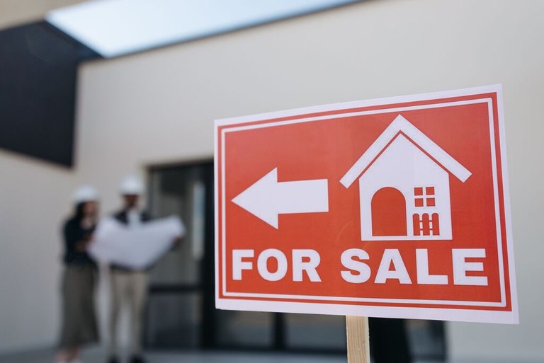 For sale sign with two people reviewing plans behind it